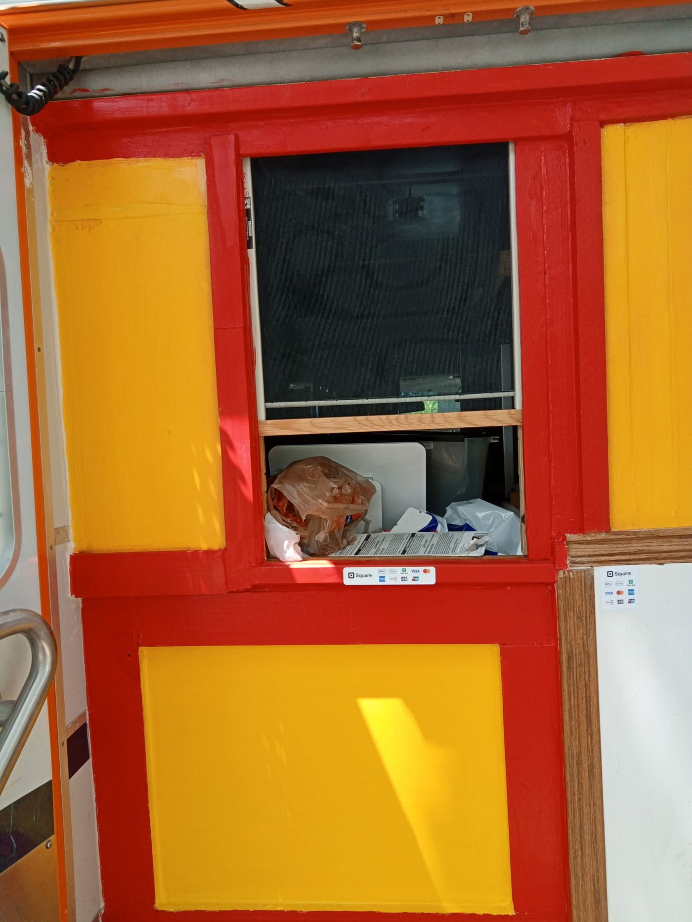 Emergency BBQ food trailer serving window painted bright red and yellow, with Square card-payment stickers